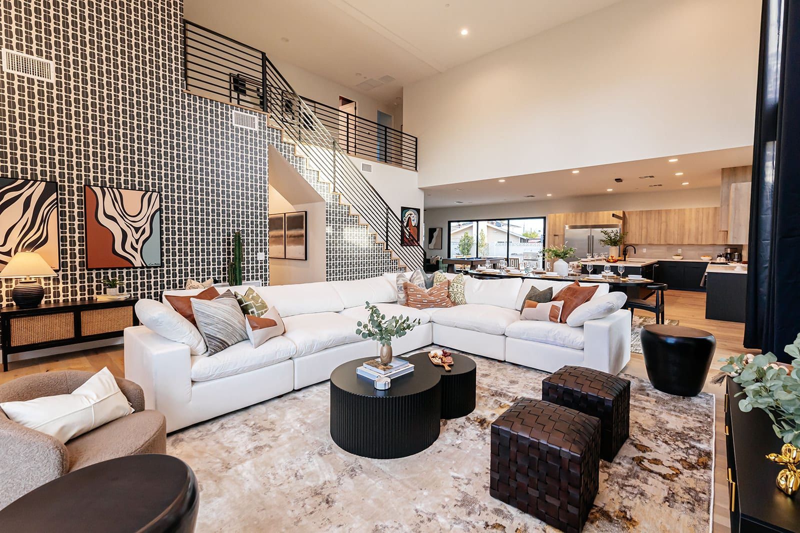 Bright modern living room with white sofas, black coffee tables, patterned rug, and staircase railing above
