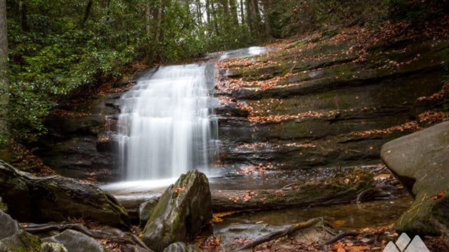 Waterfall cascading over layered rock into a pool; fall foliage surrounds.