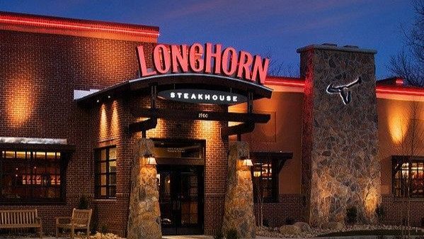Longhorn Steakhouse exterior, lit at dusk, red sign above entrance, brick and stone facade.