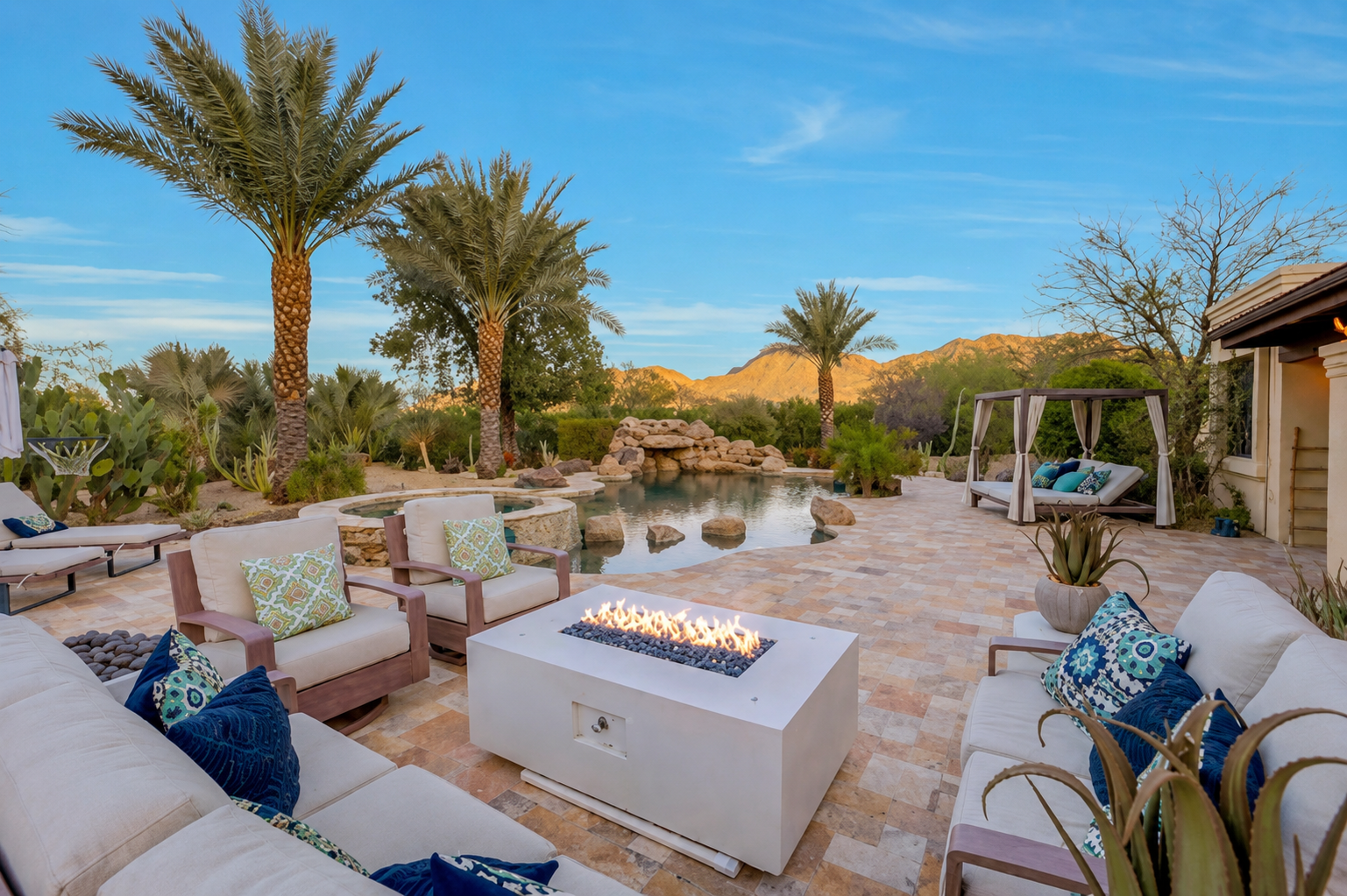 Desert patio lounge with cushioned seating, fire pit, palm trees, and mountain views at sunset