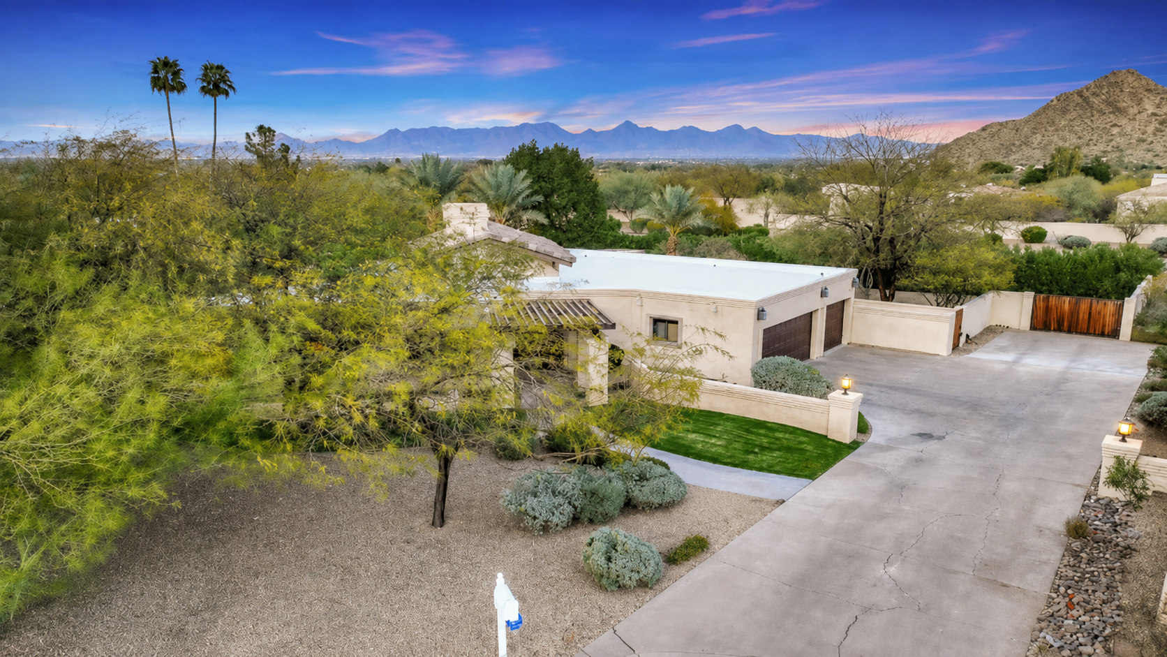 Desert home with driveway, trees, and mountains under a clear blue sky