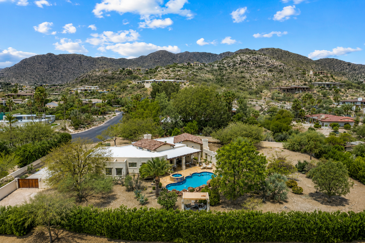 Desert home with a turquoise pool, surrounded by trees and mountains under a blue sky