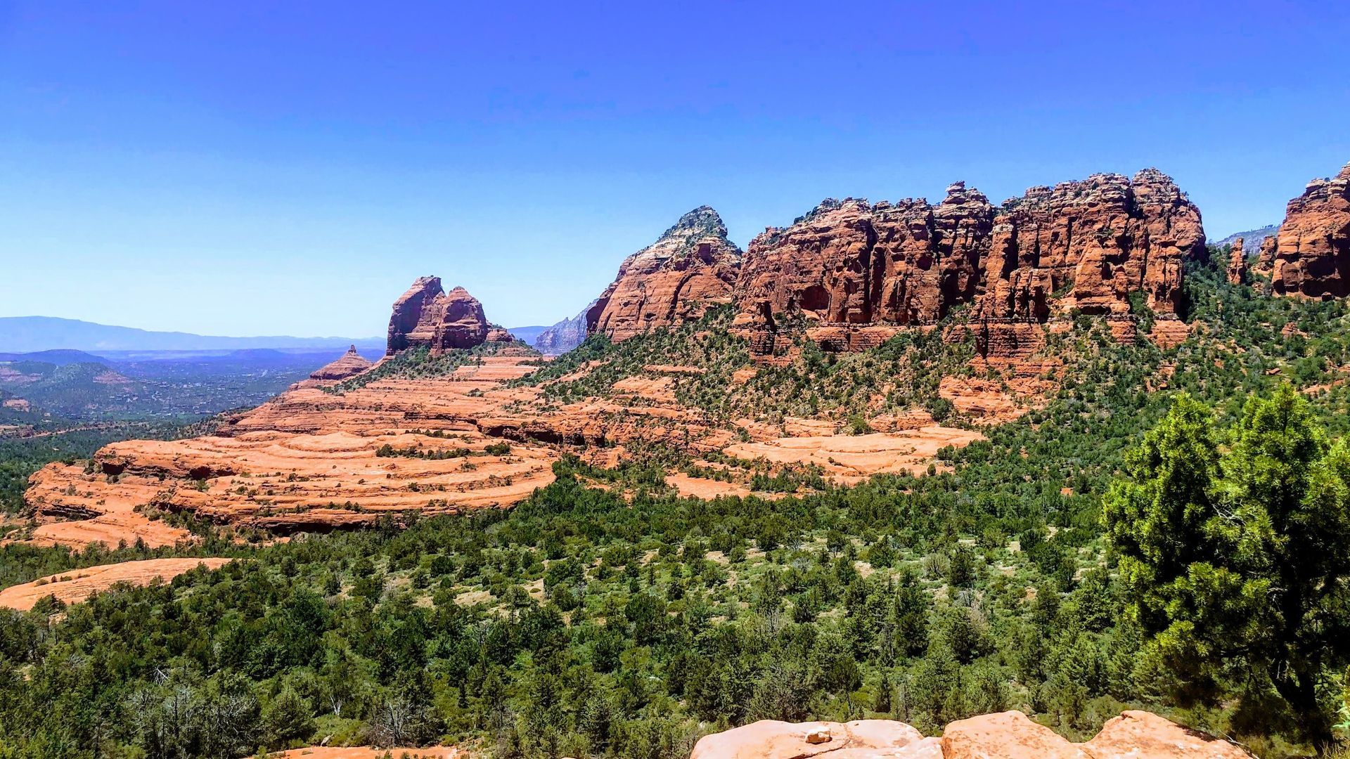 Red rock formations in Sedona, Arizona, with blue sky and green trees.