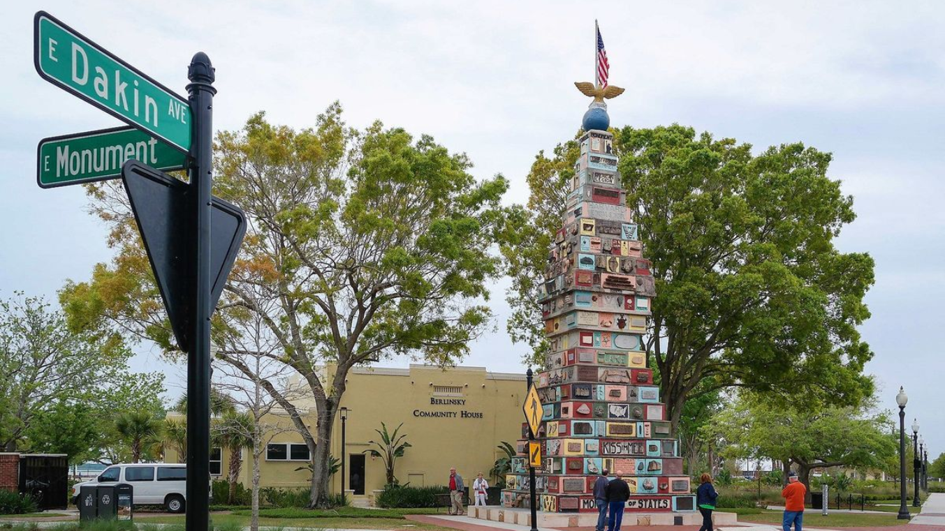 A tall sculpture made of colorful tiles at a street corner, with street signs and people in the background.