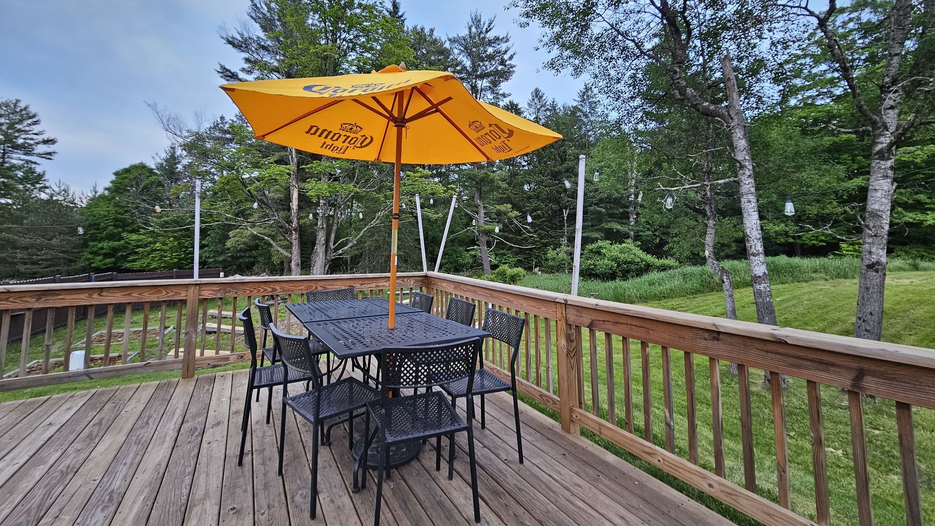Patio with black table, chairs, yellow umbrella, on a wooden deck overlooking greenery.