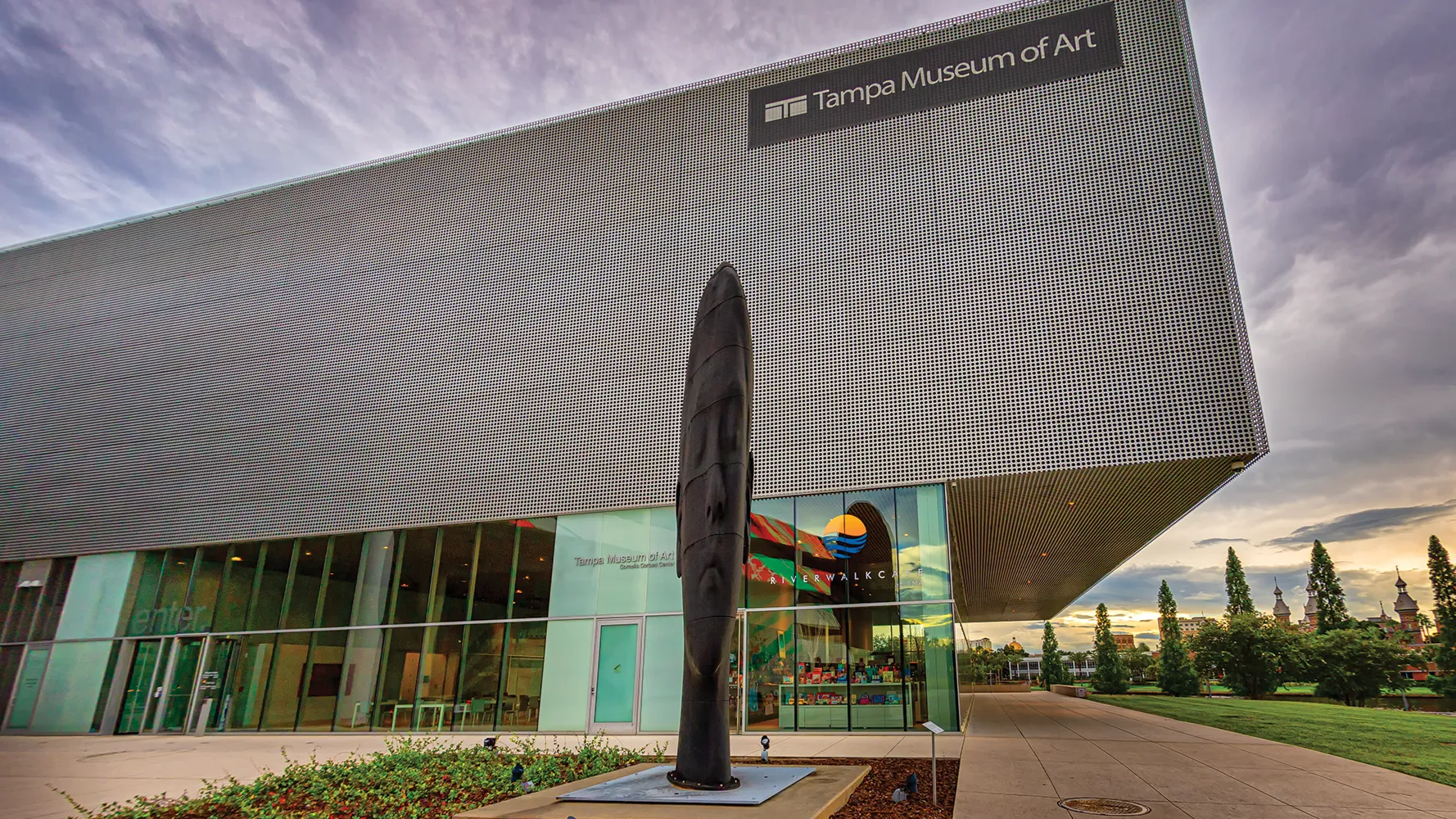 Tampa Museum of Art, modern architecture with wavy facade, outdoor sculpture in front, sky in background.