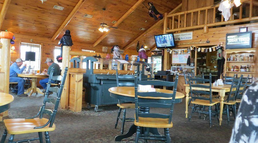 Interior of a rustic restaurant with wooden walls, tables, and chairs. People are seated at tables.