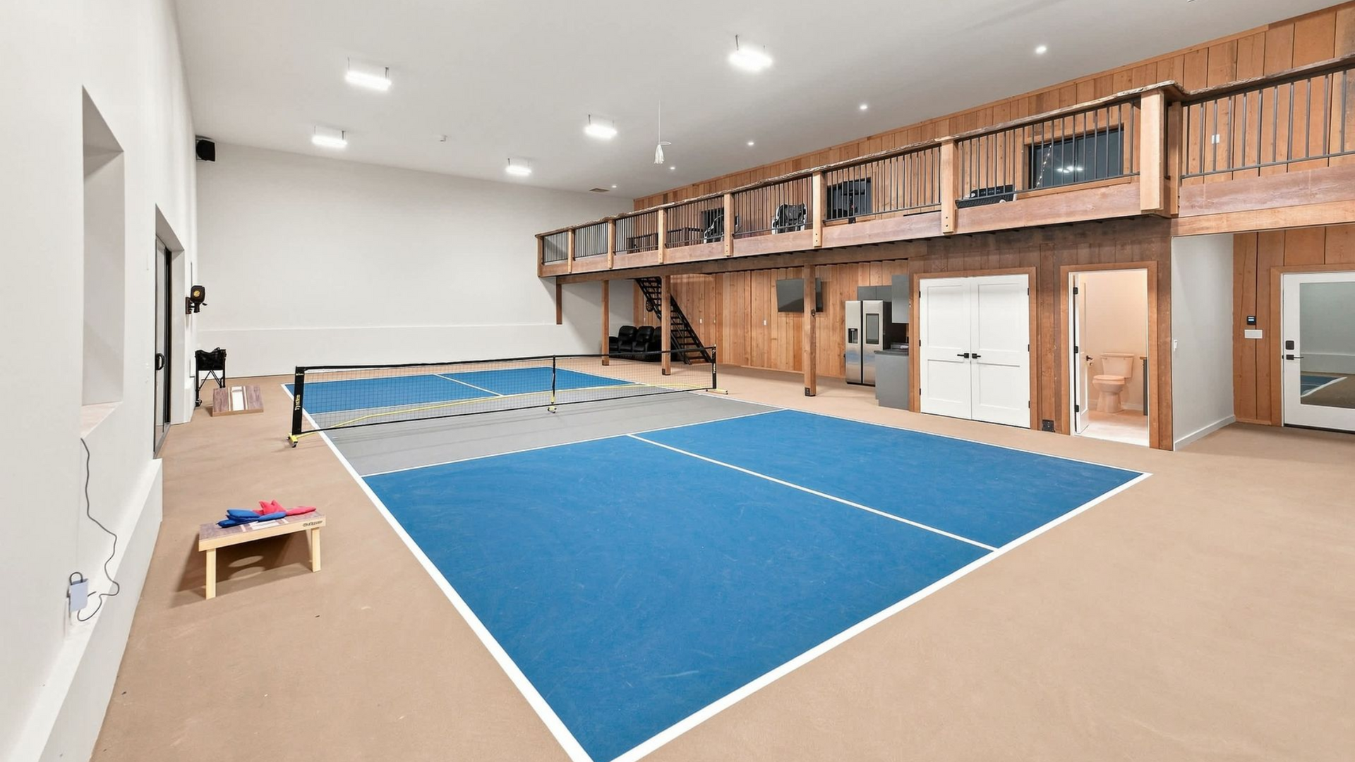 Indoor gymnastics gym with blue mats, balance beam, and loft viewing area