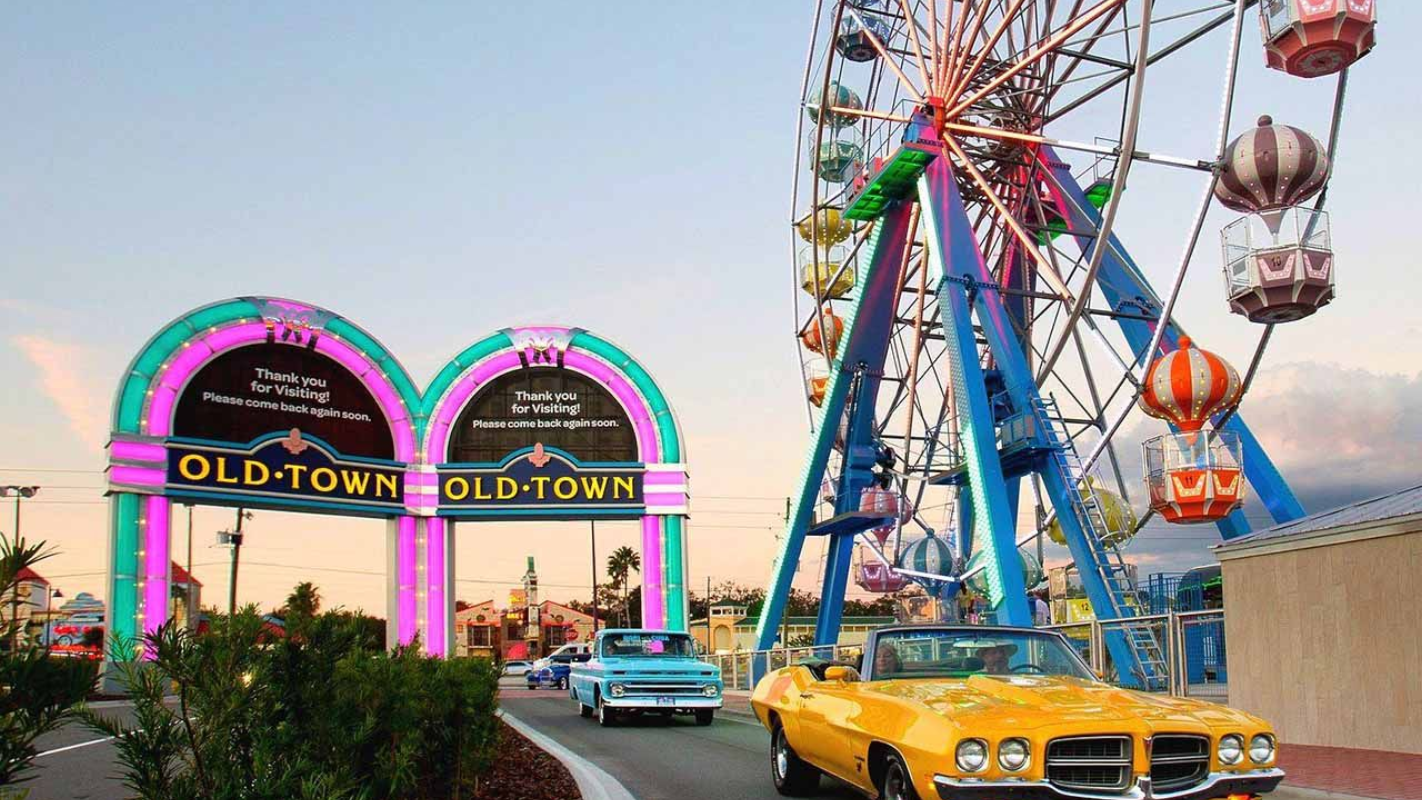 Old Town amusement park entrance with classic cars, Ferris wheel, and colorful neon lights.