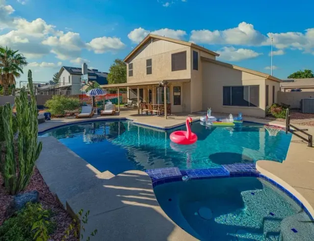 A large swimming pool with a pink flamingo float in it in front of a house.