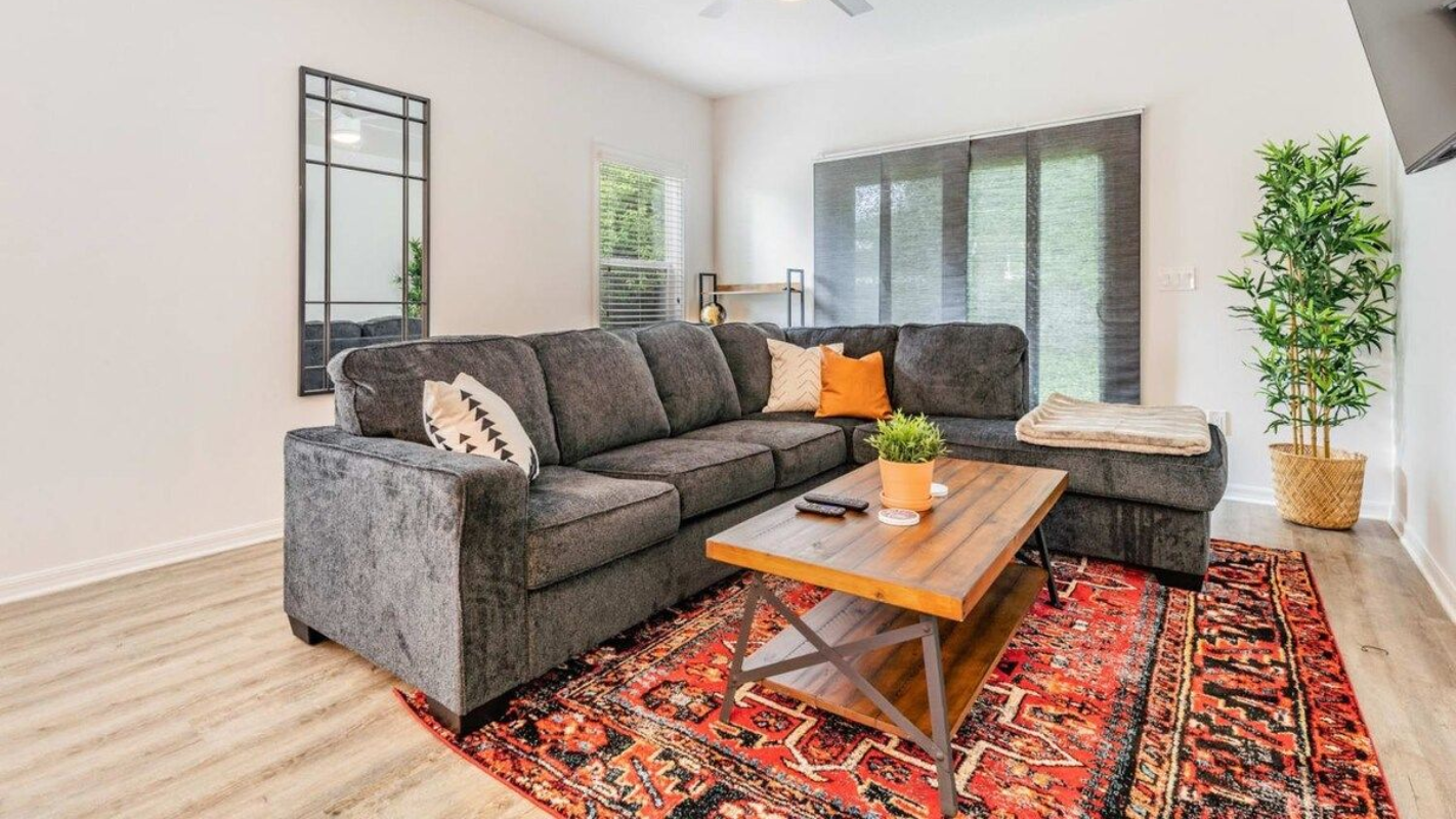 Living room with gray sectional sofa, red rug, wooden coffee table, and large mirror.