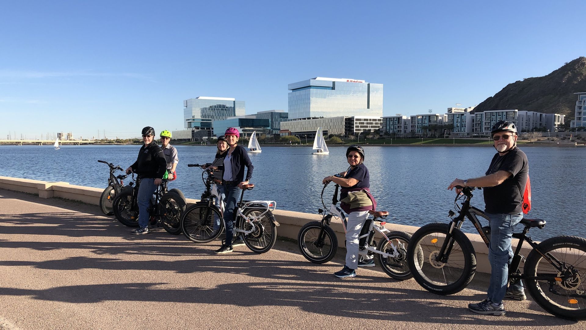 People on bikes by a lake with buildings in the background. Sunny day.