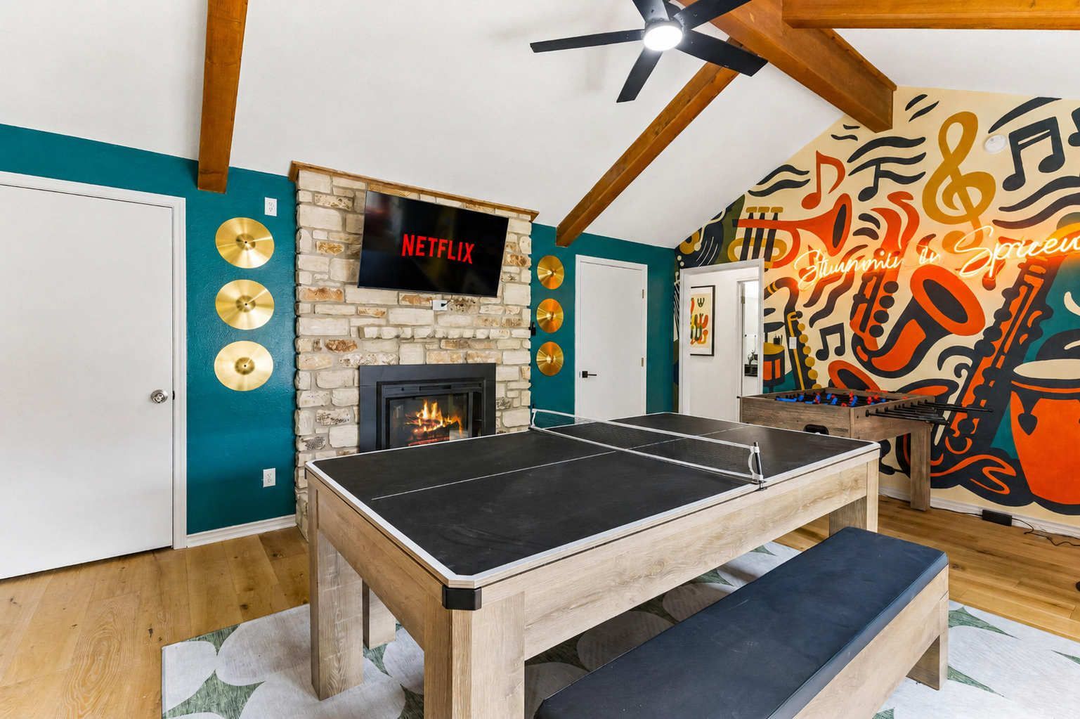 Cozy game room with stone fireplace, mural wall, pool table, and bench under vaulted ceiling