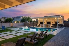 Modern backyard with pool, lounge chairs, and a lit patio at sunset