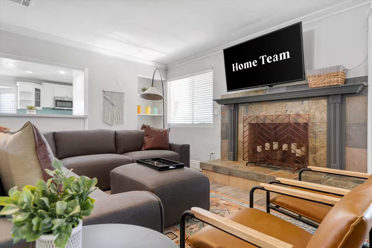 Cozy living room with brown sectional, fireplace, and TV displaying “Home Team”