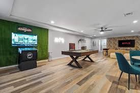 Modern basement game room with TV, pool table, dartboard, and lounge seating on wood floors