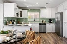 Bright white kitchen with green backsplash, stainless appliances, and a breakfast table in the foreground