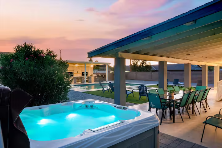 Backyard patio at dusk with a glowing hot tub, dining table, chairs, and sunset sky