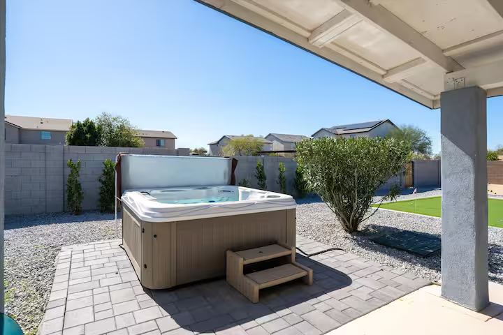Backyard patio with a covered hot tub, paver stones, shrubs, and a blue sky