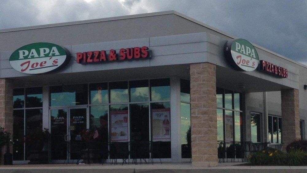 Papa Joe's Pizza & Subs storefront with green and red signage. Beige brick accents, glass windows.
