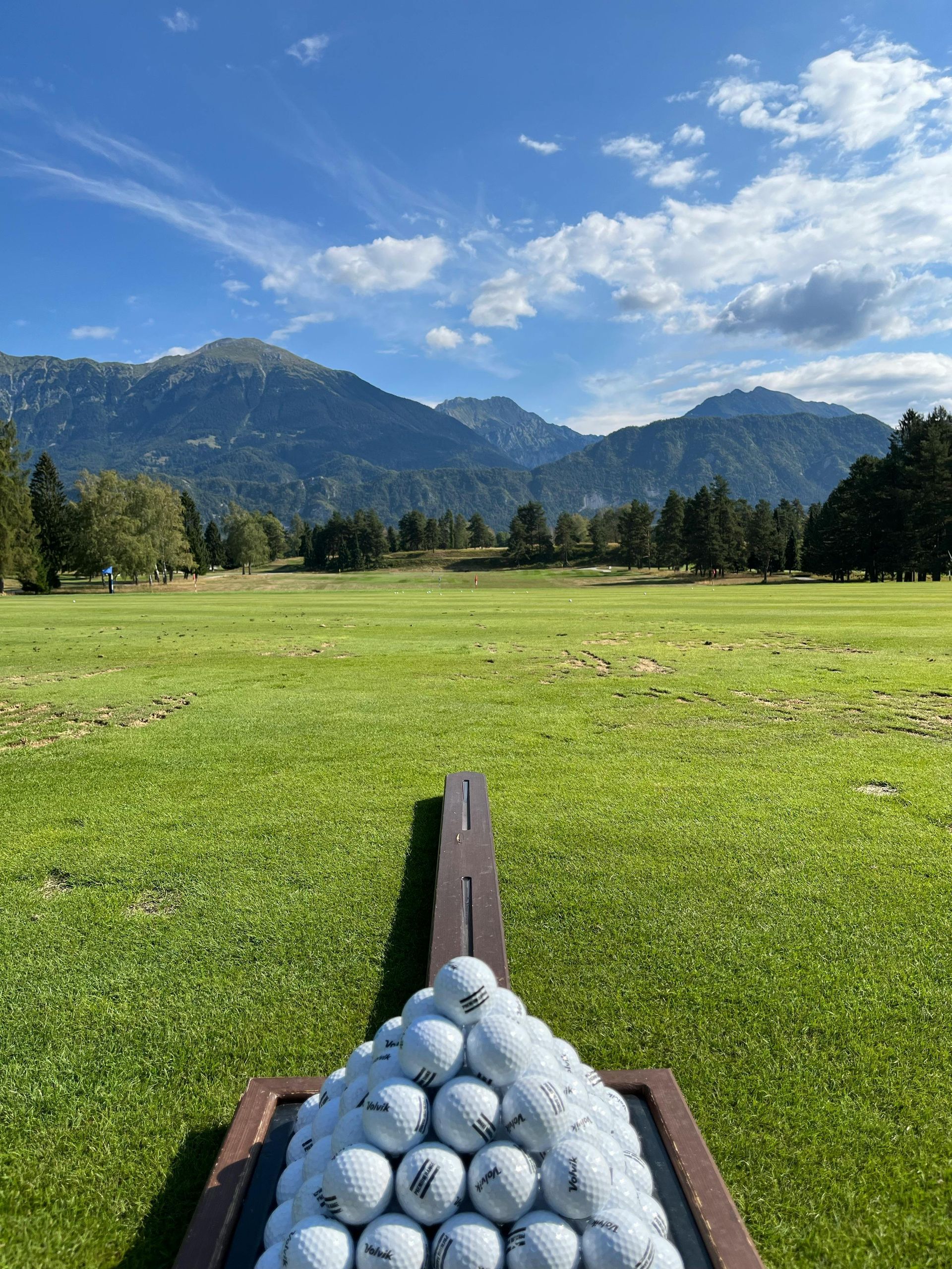 A pile of golf balls on a golf course with mountains in the background.