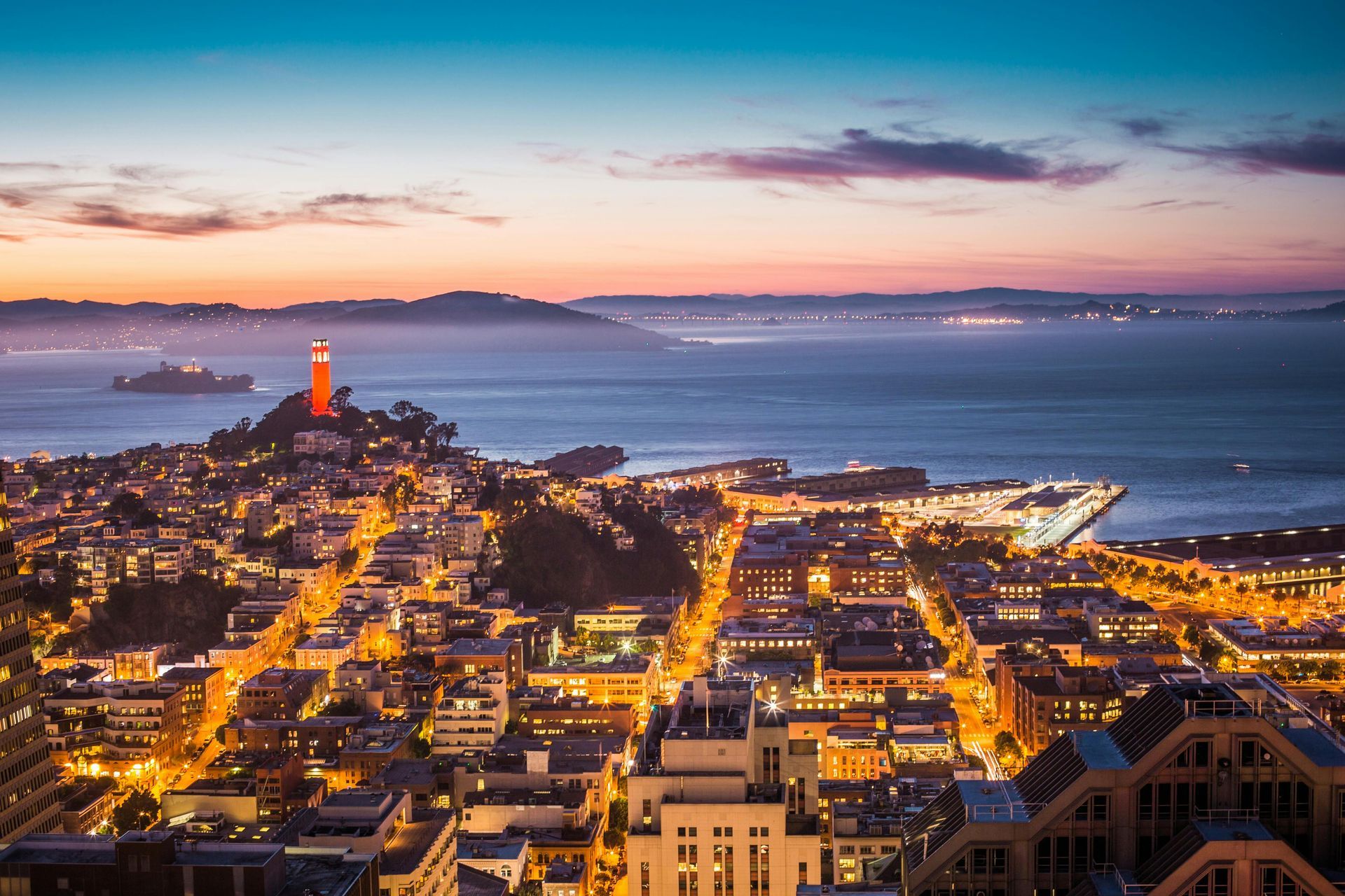 An aerial view of San Diego, CA at night with a lighthouse in the distance.