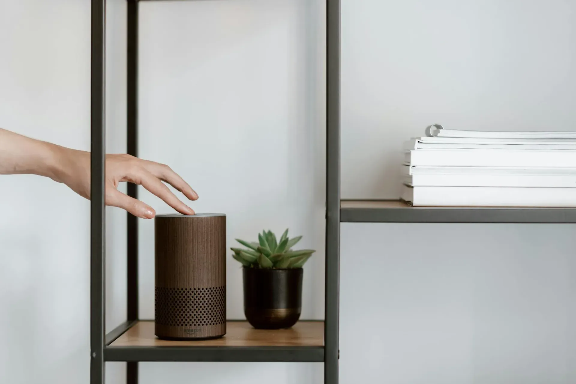 A person is reaching for an amazon echo speaker on a shelf.