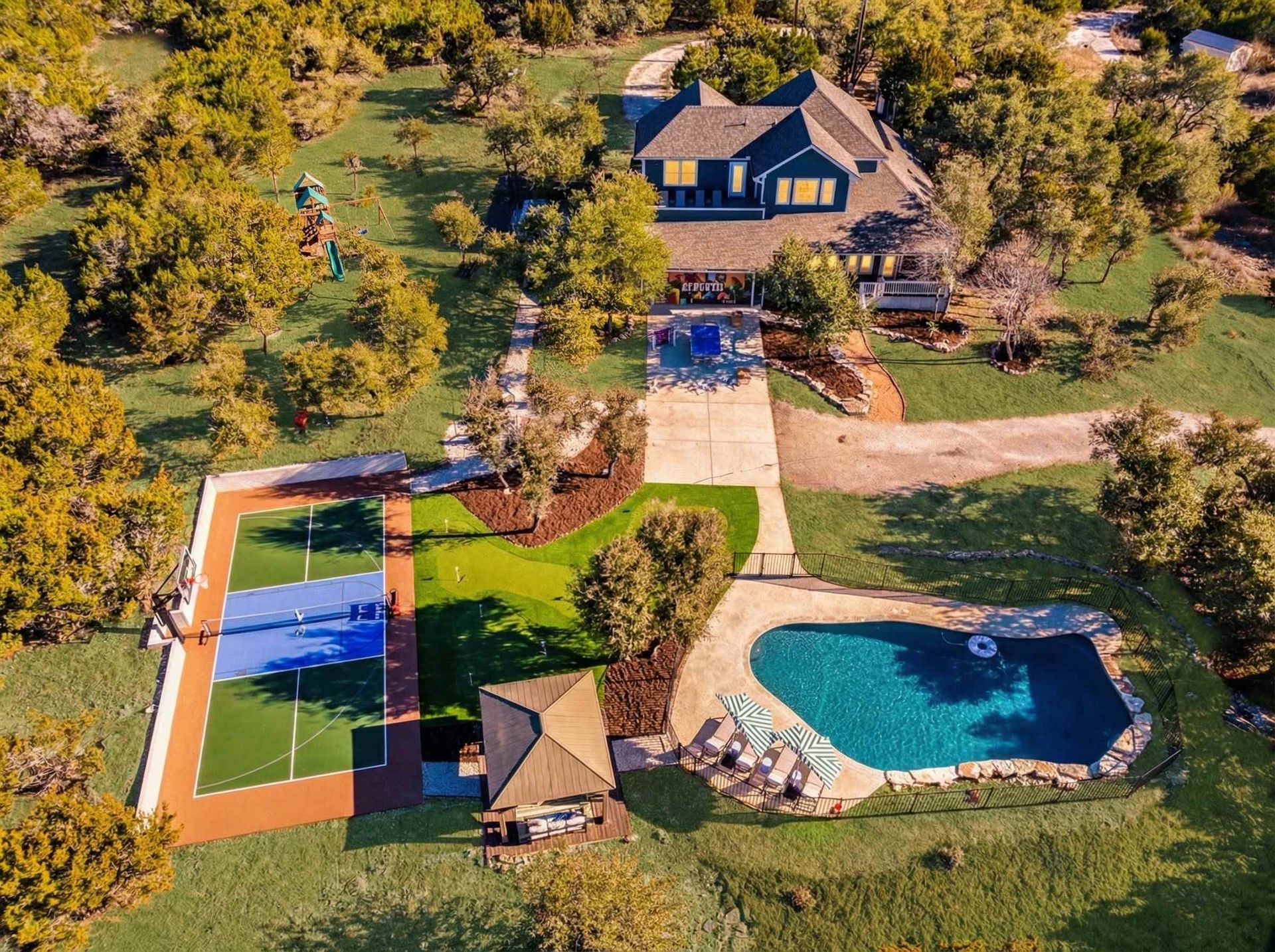 Aerial view of a countryside home with pool, lawn, tennis court, and trees