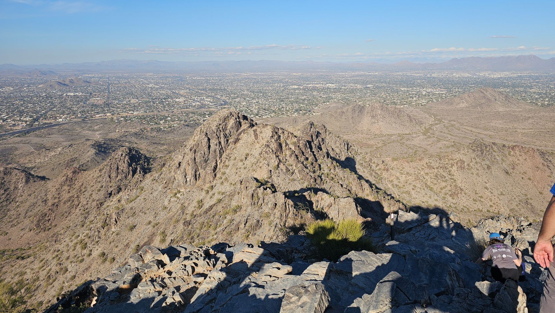 View from a rocky mountain summit, overlooking a sprawling city under a hazy sky.
