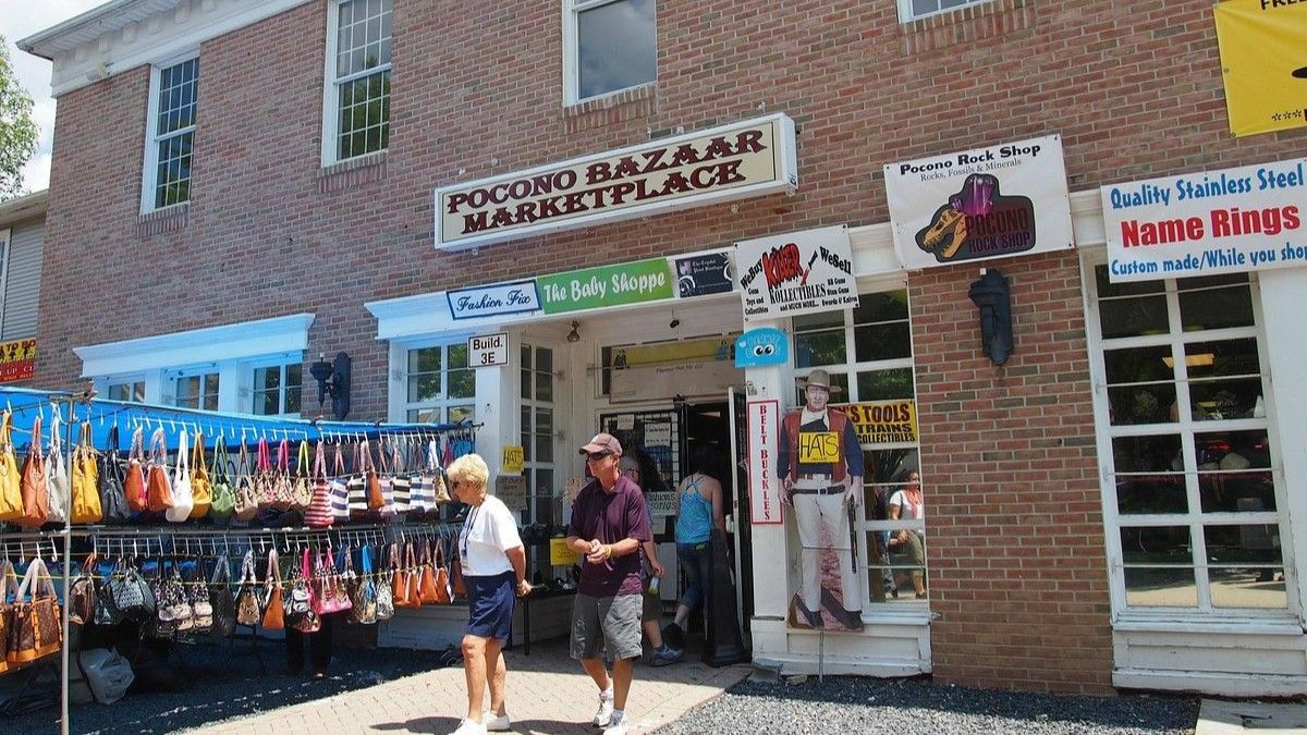 Pocono Bazaar Marketplace exterior; people walking; bags for sale; brick building, white trim.