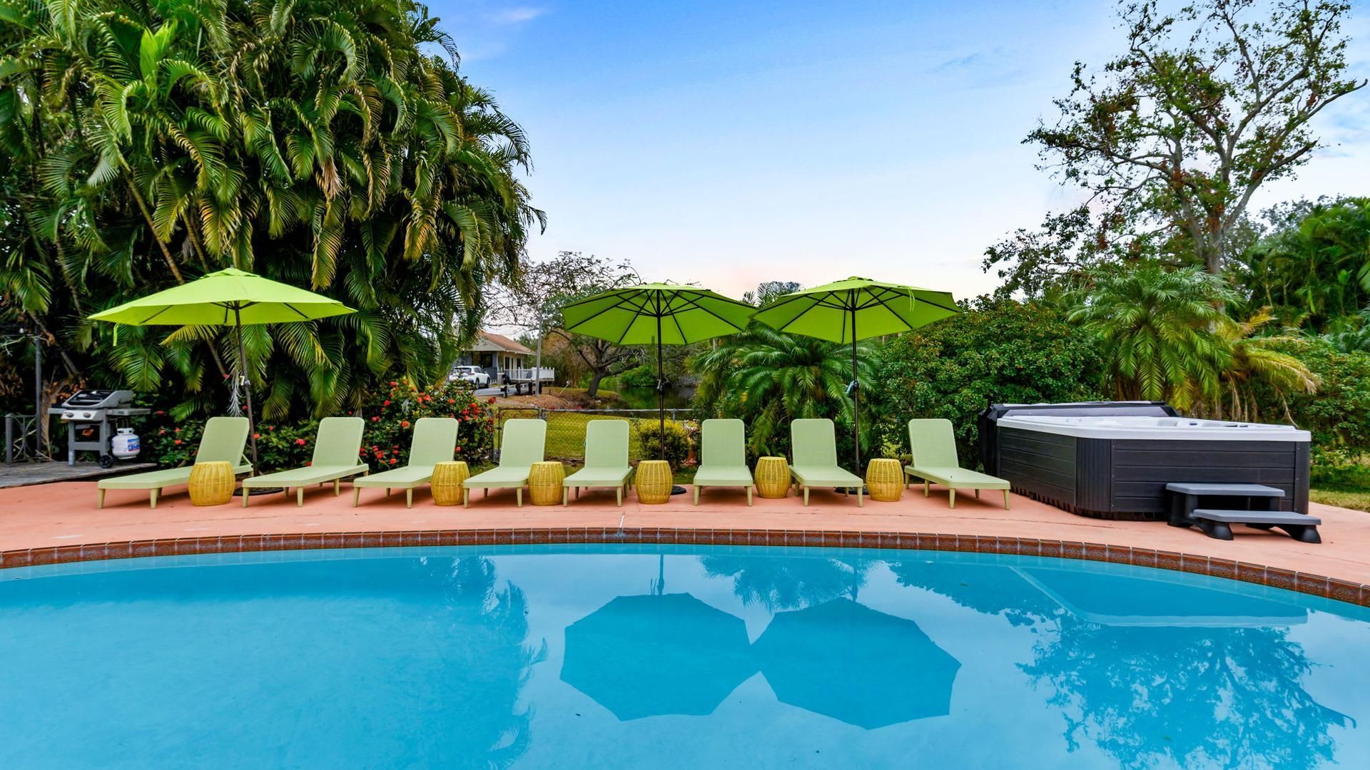 Private pool and hot tub oasis Luxury outdoor pool area with lounge chairs, green umbrellas, tropical landscaping, and private hot tub
