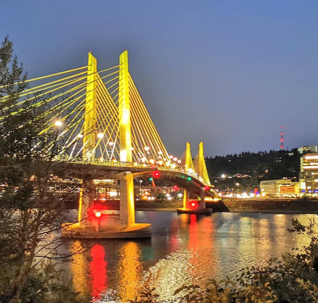 Tilikum Crossing (Bridge of the People) lit in a yellow hue against a dark sky