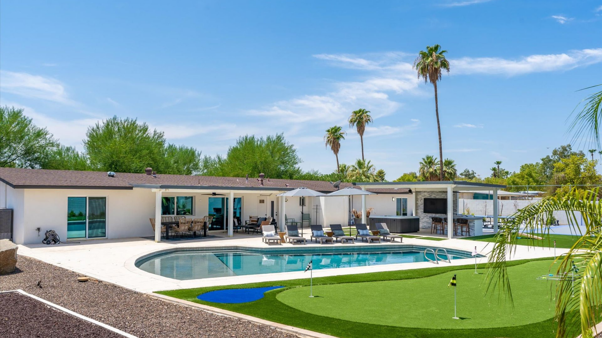 Modern house with a backyard pool, patio seating, and palm trees under a bright blue sky