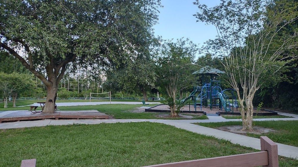 Park scene with playground, trees, walkway, and green grass.