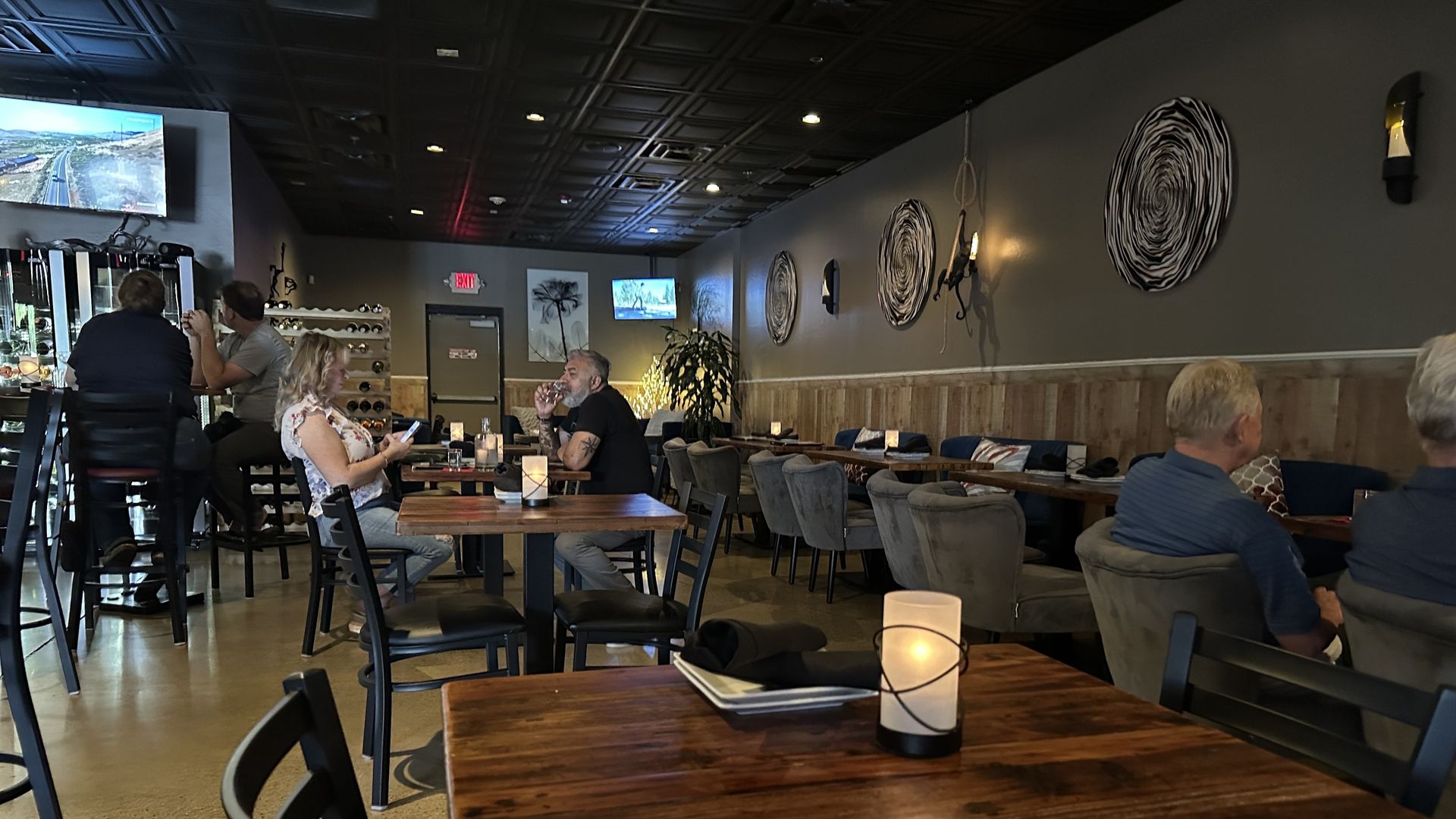 Restaurant interior: patrons seated at tables, bar area in the background, dimly lit with decorative wall art.