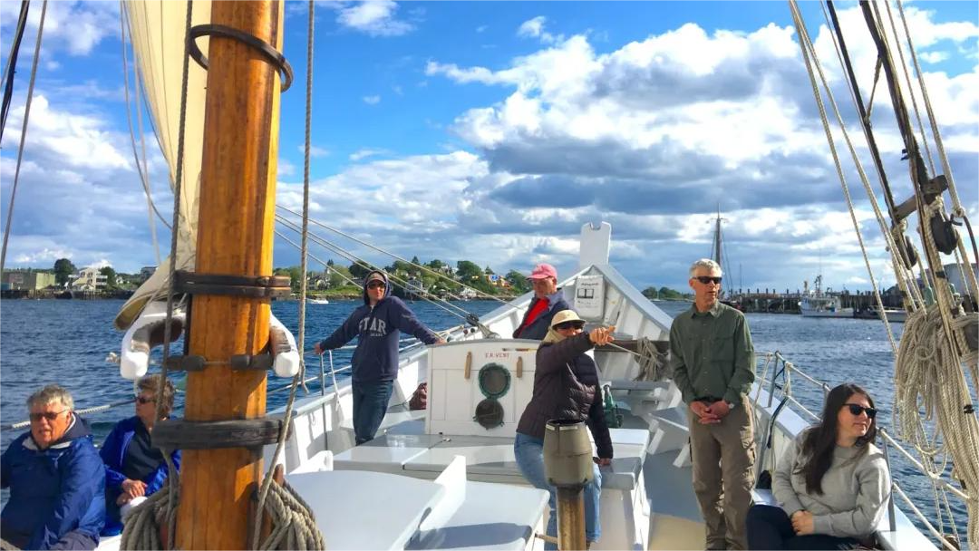 People sailing on a boat under a partly cloudy sky, some standing and looking out.