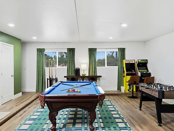 Game room with pool table, arcade machines, and a foosball table on a patterned rug
