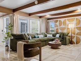 Cozy living room with green sectional, wood-beam ceiling, large windows, and patterned accent wall.