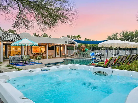 Backyard pool and hot tub beside a patio at sunset, with lounge chairs and umbrellas