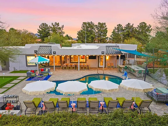 Outdoor resort pool with white umbrellas, lounge chairs, and a bar at sunset