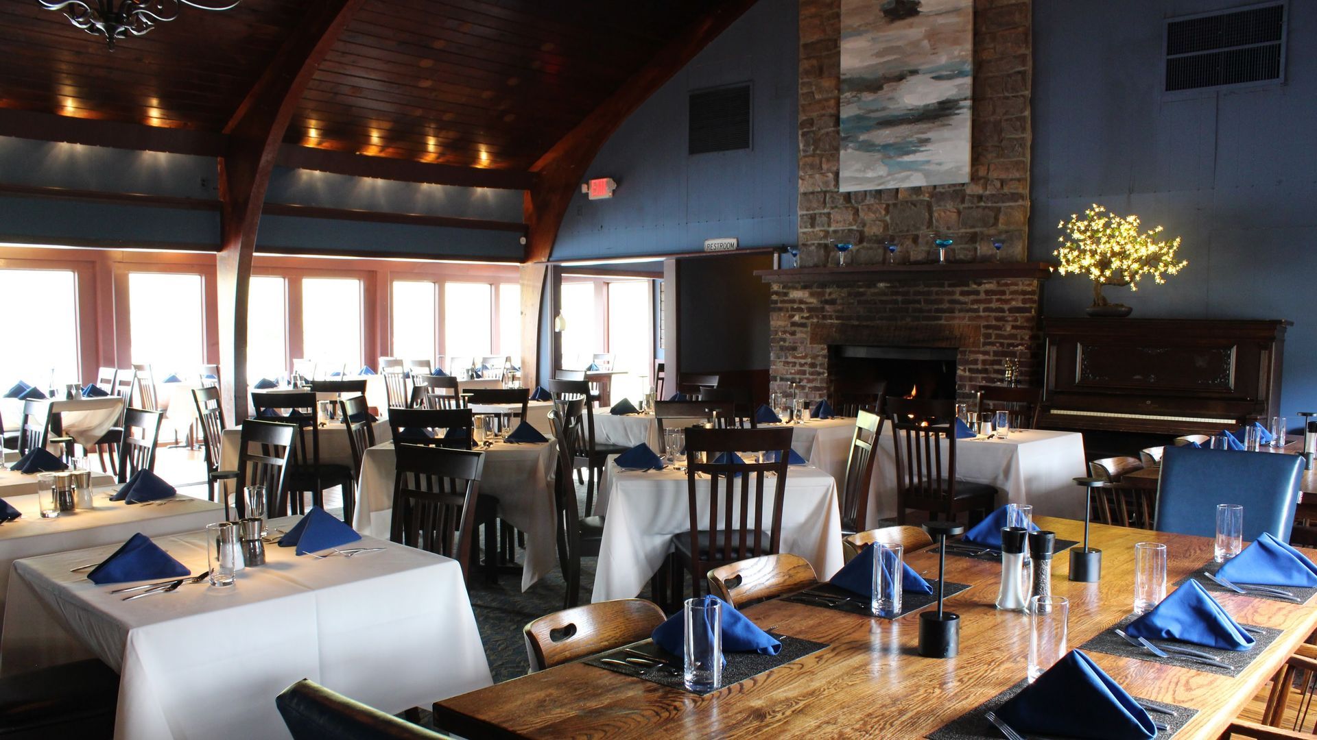 Restaurant interior with tables set for dining, fireplace, and piano.