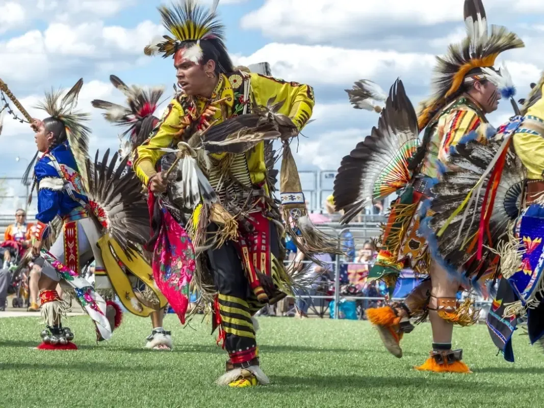 A group of people in native american costumes are dancing on a field at the Arizona Indian Festival