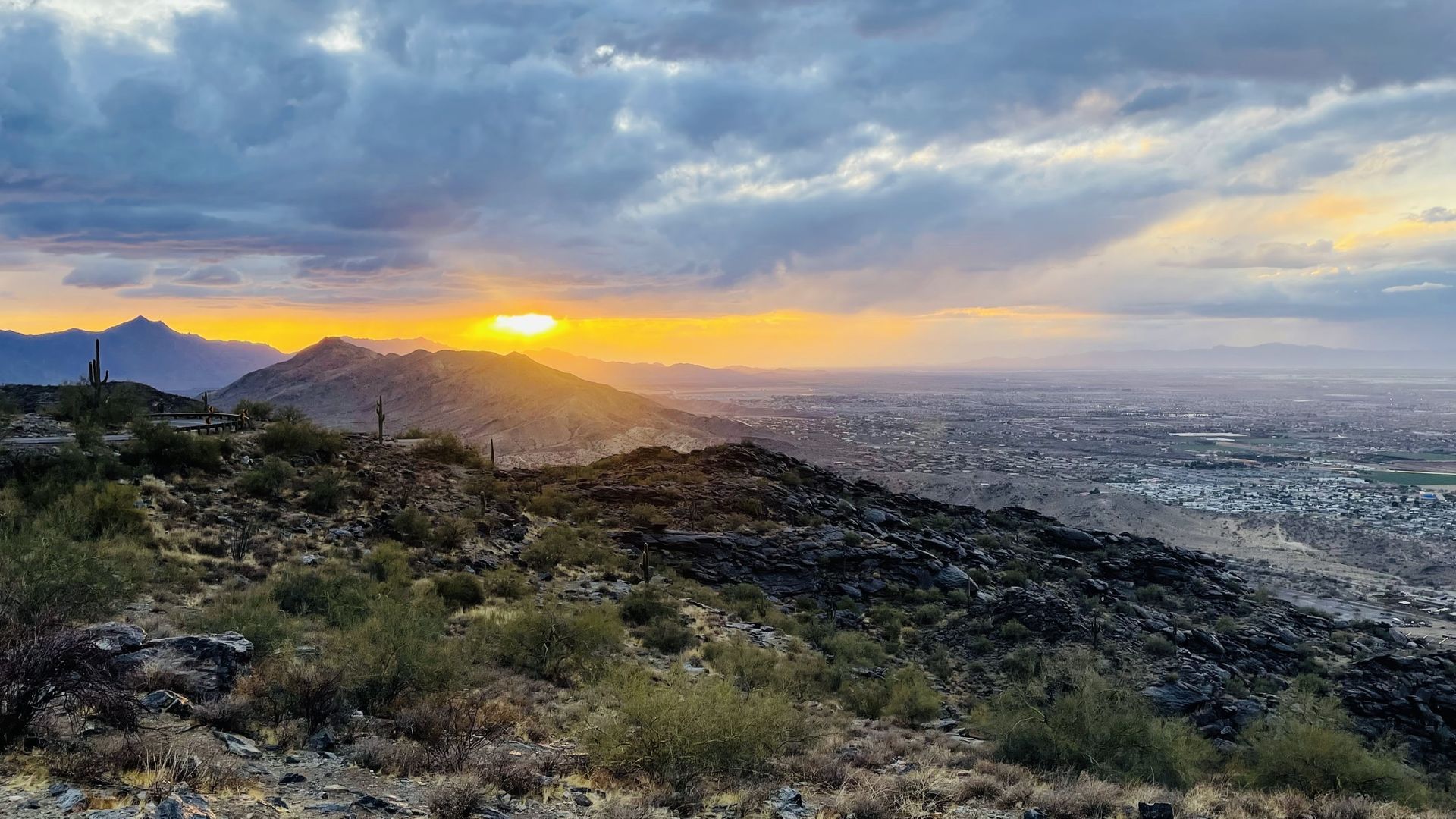 Sunset over a mountainous landscape with a city in the distance, dramatic sky with sunbeams.