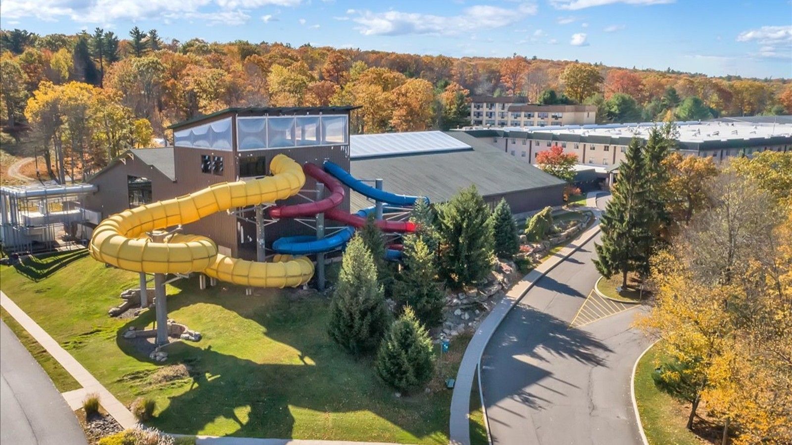 Waterpark with yellow, red, and blue slides. Building with trees in the background.