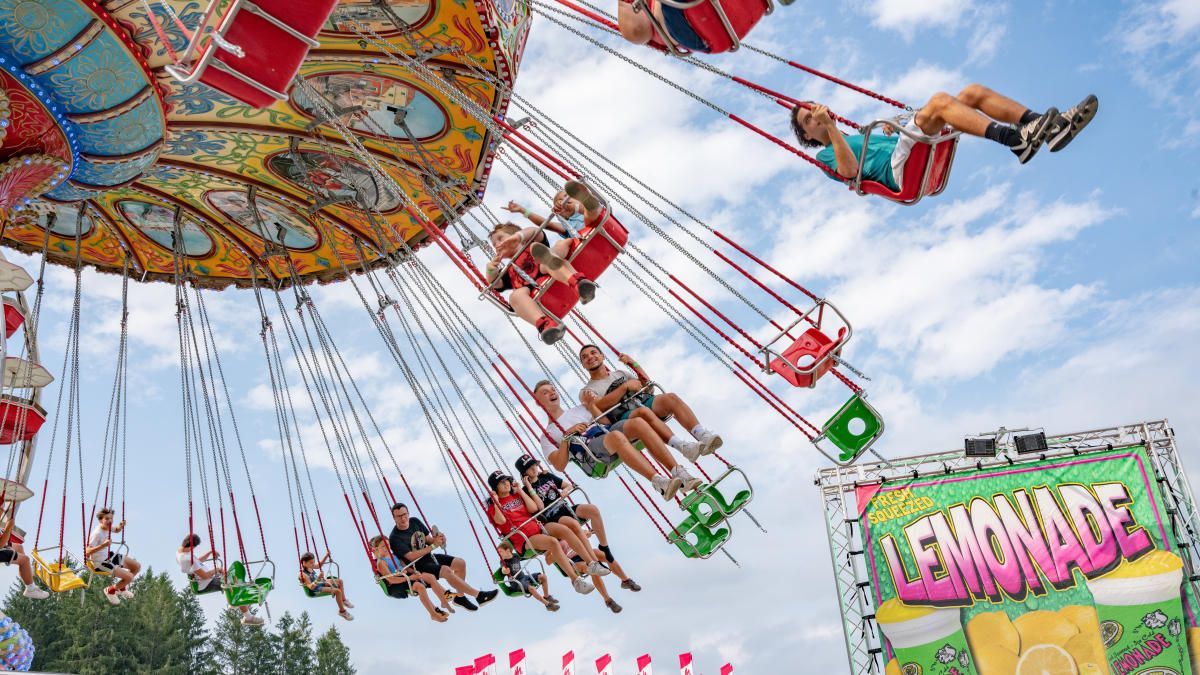 People on a carnival swing ride against a blue sky, near a 