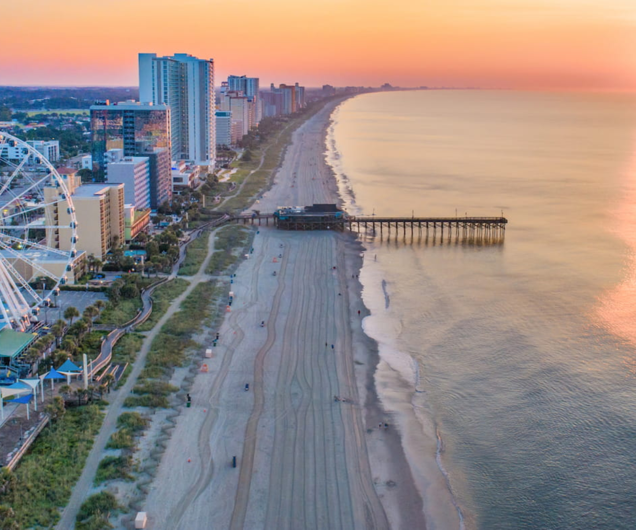 An aerial view of a beach with a pier and ferris wheel at sunset in Surfside Beach, SC