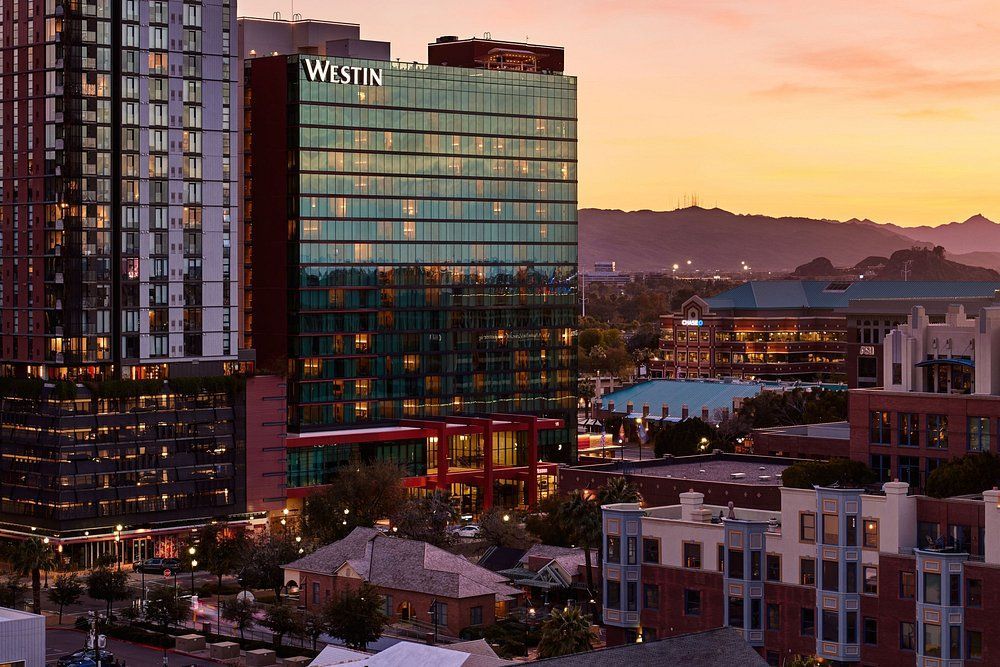 Downtown city skyline at dusk with a glass hotel tower glowing against a purple sunset