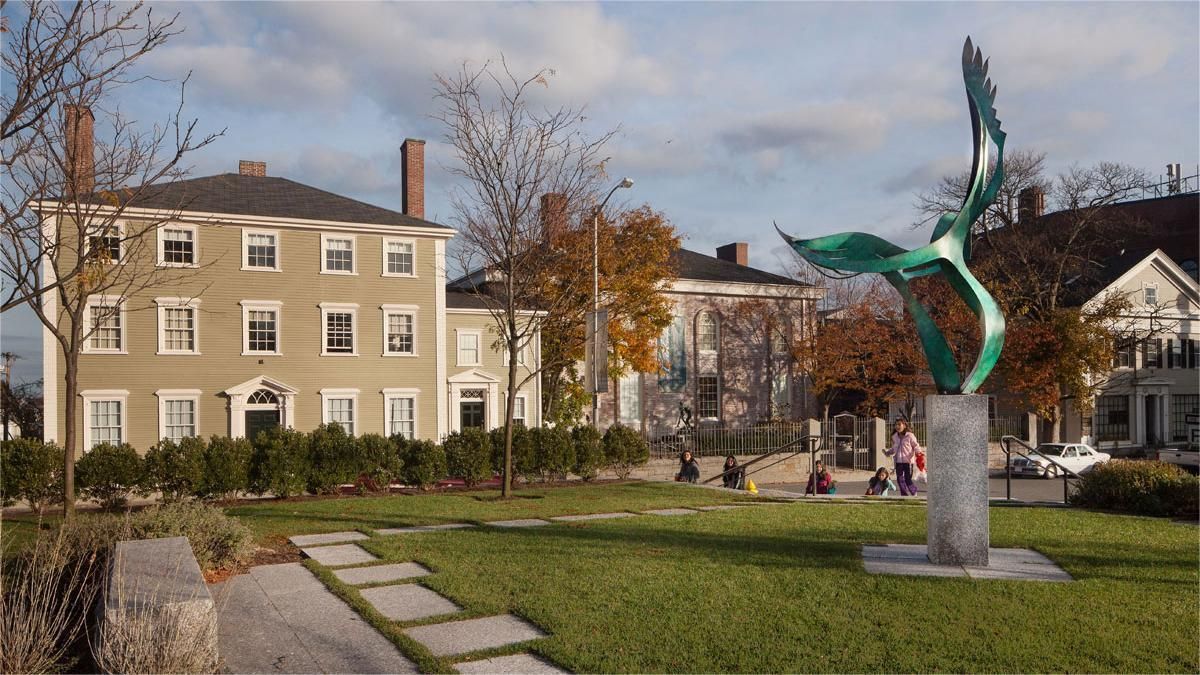 Park with sculpture, buildings, and green space under a partly cloudy sky.
