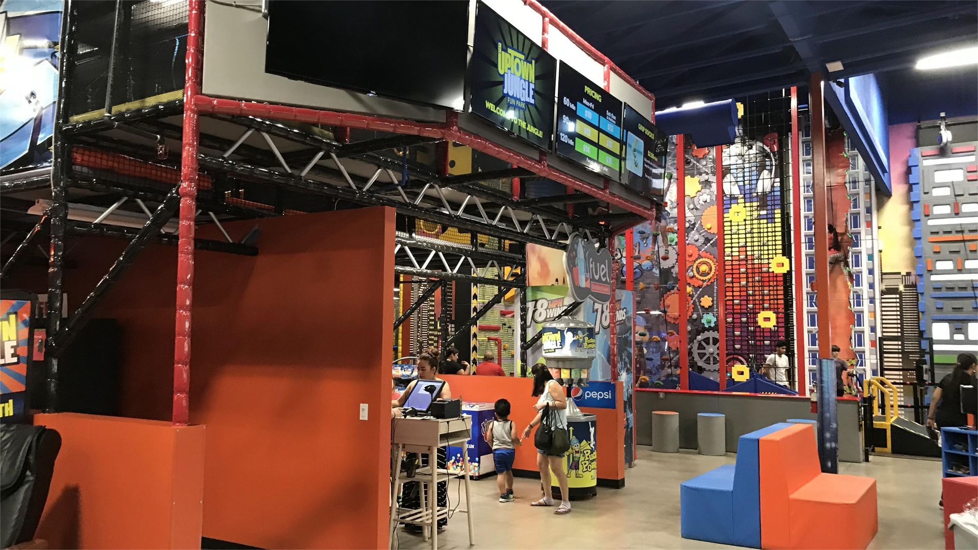 Indoor adventure park, orange and blue walls with climbing structures, people entering.