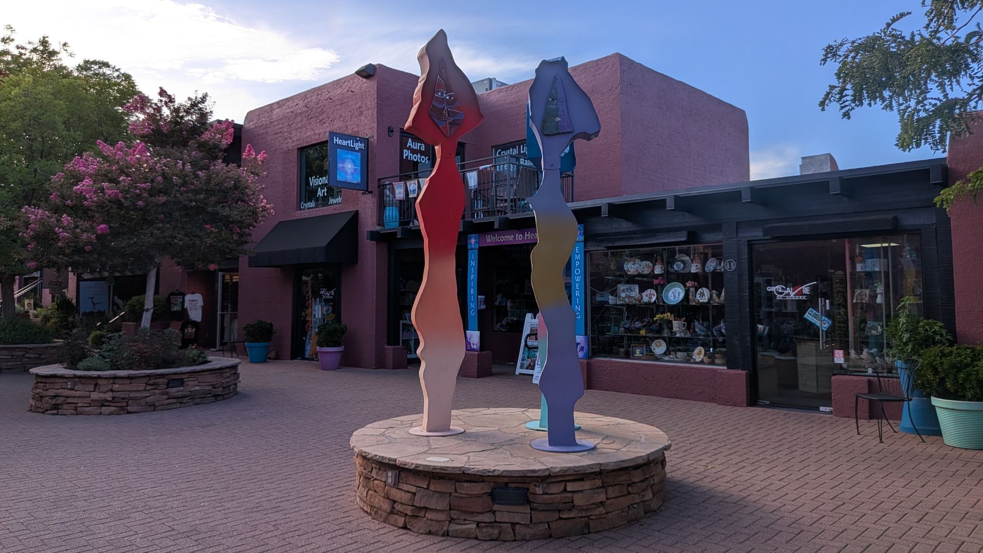 Sculptures in plaza with shops and pink adobe buildings.